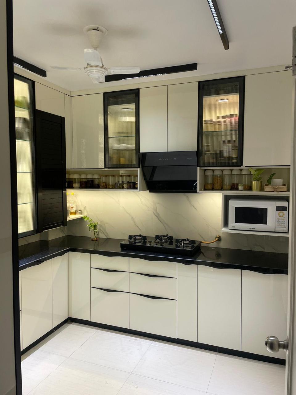 Cream modular kitchen with black fluted glass upper cabinets and marble backsplash